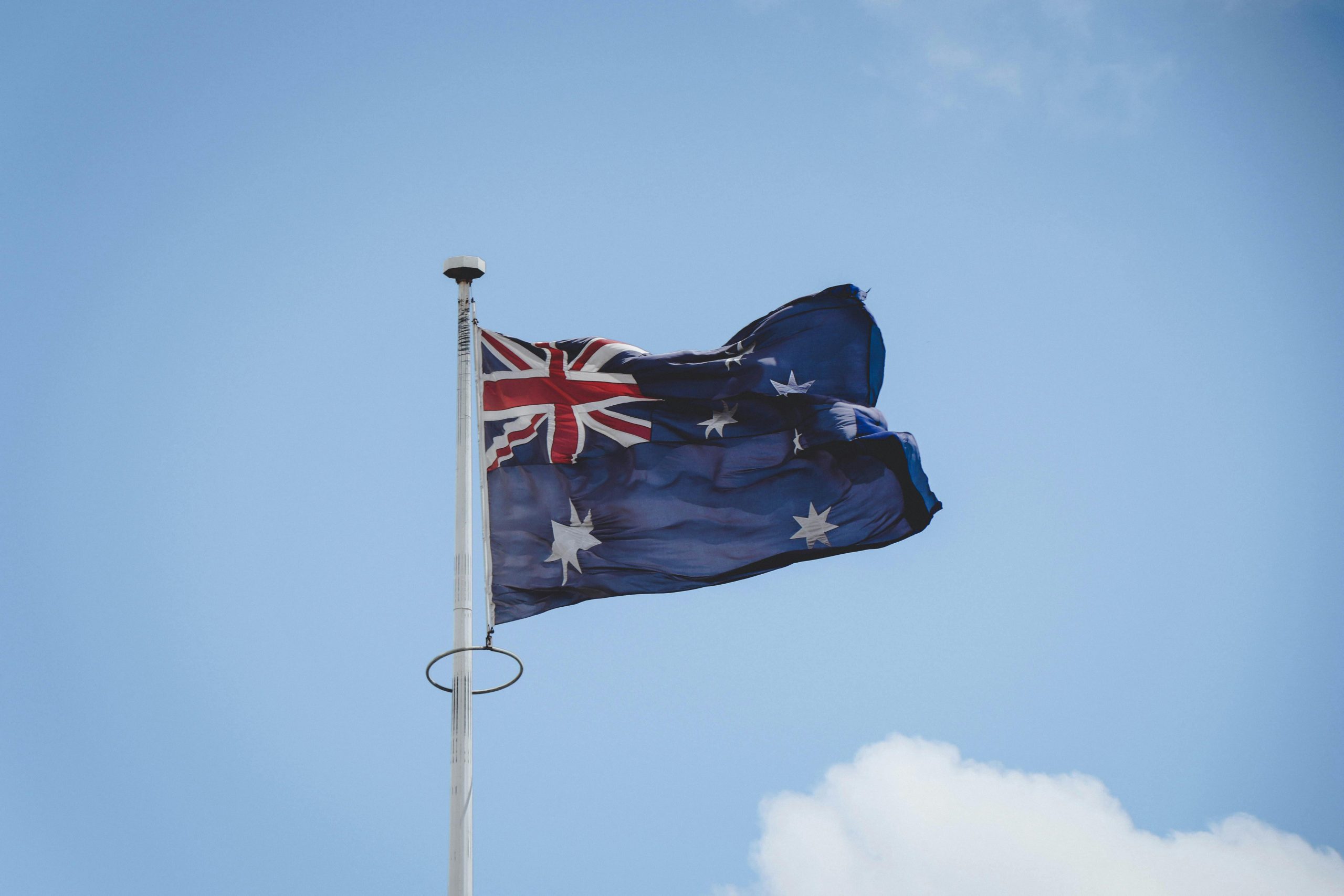 Authentic Company for Immigration to Australia from Dubai Australian national flag waving on a flagpole against a clear blue sky in Perth.