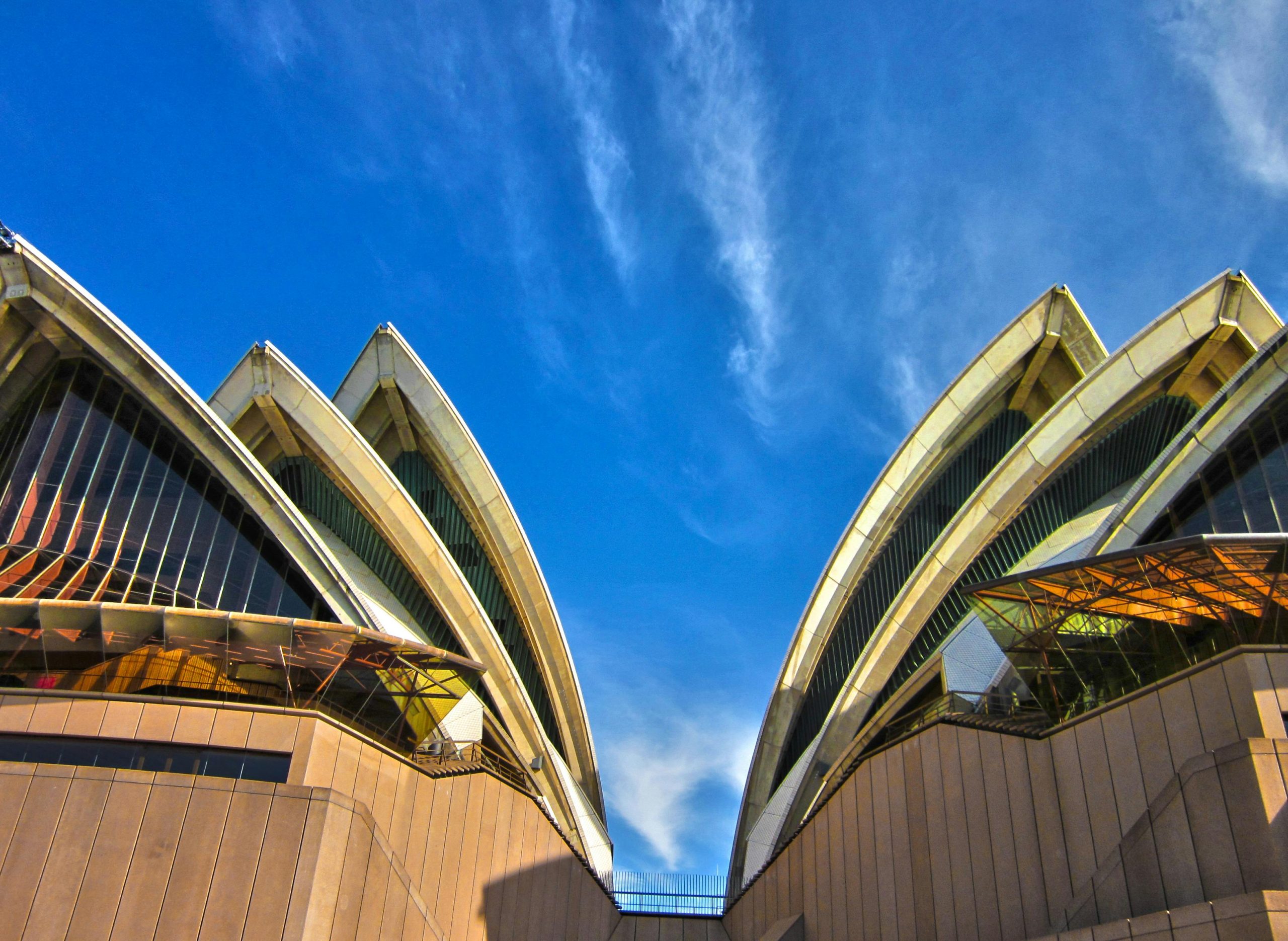 A striking low angle view of the iconic Sydney Opera House with a vibrant blue sky background, showcasing its modern architectural design.